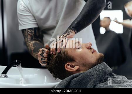 Attraktiver Mann bekommt einen modernen Haarschnitt im Friseurladen. Draufsicht auf einen jungen Mann, der seine Haare gewaschen und seinen Kopf in einem Friseursalon massiert Stockfoto