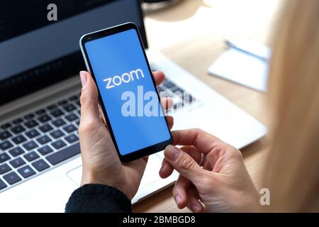 Zoom-App für Smartphone. Frau mit Telefon in den Händen und einem Logo der Videokonferenz-Anwendung auf dem Bildschirm dieser. Stockfoto