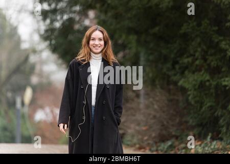 Junge Frau trägt Wollmantel in Park lächelnd Stockfoto