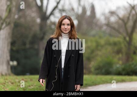 Junge Frau trägt schwarzen Mantel posiert im öffentlichen Park Stockfoto