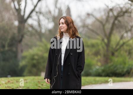 Junge Frau trägt lange schwarze Wolle Mantel im Park wegschauen Stockfoto