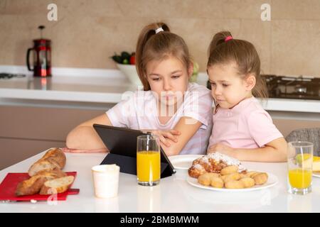 Zwei Schwestern beim Frühstück und beim Ansehen von Cartoons auf einem Tablet zusammen, glückliches Familienkonzept Stockfoto
