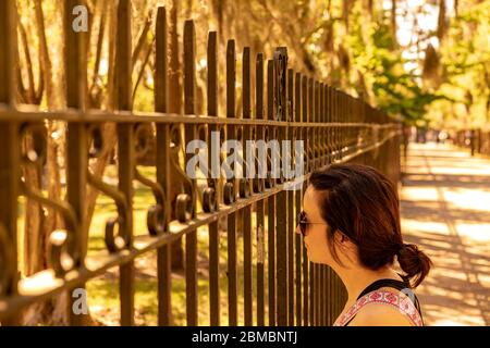 Eine Frau mit Sonnenbrille zieht durch einen Zaun. Stockfoto