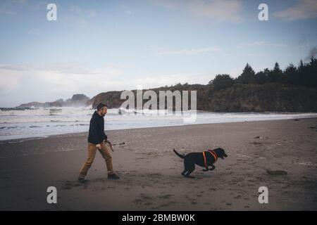 Ein Mann spielt mit einem Hund auf dem Kalifornier Strand Stockfoto