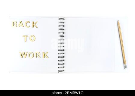 Die Inschrift "Back to work" aus Holzbuchstaben, die auf einem offenen Notizbuch mit weißen Seiten liegen, isoliert auf weißem Hintergrund mit einem Schnittpfad. Stockfoto