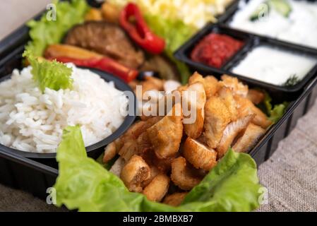 Traditioneller Döner Kebab in einem schwarzen Plastikbehälter, saure Sahne, weiß gekochter Reis, Braten, Chiken, Saucen, Salat, Kohl und gebratenes Gemüse Stockfoto