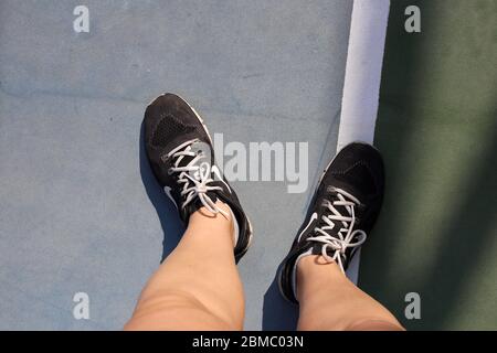 Gebräunte junge kaukasische Frau, die während eines sonnigen Urlaubstages in Dubai, Vereinigte Arabische Emirate, im Januar 2020 schwarze Nike Free Sneaker auf einem Tennisplatz trägt. Stockfoto