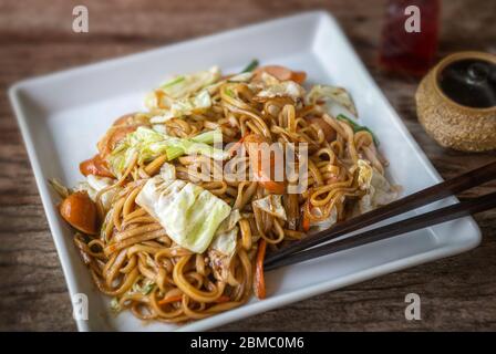 Yakisoba mit Wurst japanischen Stil gebratene Nudeln mit süßer Sauce in weißen Teller mit schwacher Sonneneinstrahlung. Stockfoto