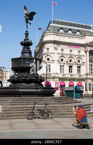 Mann fotografiert sein faltbares Carrero Fahrrad Fahrrad vor dem weltberühmten Shaftesbury Memorial Fountain & Statue von Anteros – fälschlicherweise als Eros bekannt – mit einem sonnigen blauen Himmel / Himmel mit Sonne an einem sonnigen Tag im Piccadilly Circus, London. GROSSBRITANNIEN (118) Stockfoto