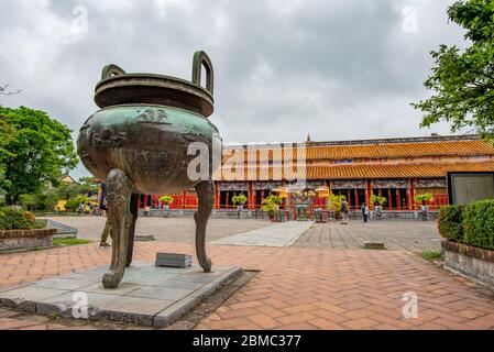 Hue, Vietnam - 15. April 2018: Eine der berühmten Urnen (Kessel) der Hue Zitadelle mit sehr wenigen Touristen und einem bewölkten Himmel Stockfoto