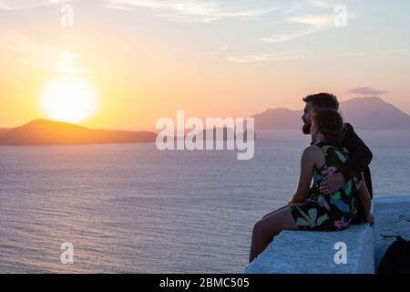 Ein junges Paar genießt einen Sonnenuntergang an der Küste in der Nähe der Thalassitra Kirche, Plaka, Milos, Kykladen Inseln, Griechenland Stockfoto