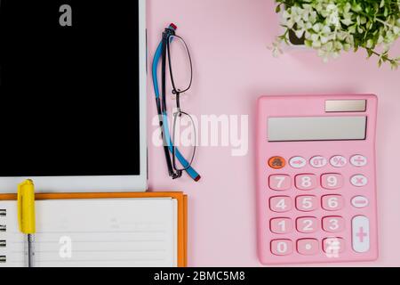 Pastellrosa Schreibtisch mit Notebook, Tablet, Brille und Taschenrechner. Draufsicht mit Kopierraum.Schreibtisch Tischkonzept. Stockfoto