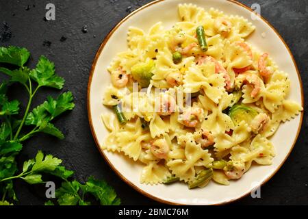Italienische Pasta in cremiger Sauce mit Garnelen auf einem Teller, Draufsicht. Farfalle mit Garnelen auf einem dunklen Tischhintergrund. Stockfoto