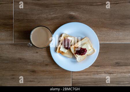 Tasse Kaffee mit Milch und zwei Scheiben gerösteten Sandwich-Brot mit Butter und Himbeer-Marmelade eine weiße Platte. Gesundes Frühstück mit Kaffee. Draufsicht Stockfoto