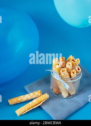 Leckere Waffelbrötchen mit Puderzucker in einer Glasschüssel Mit Luftballons auf blauem Hintergrund Stockfoto