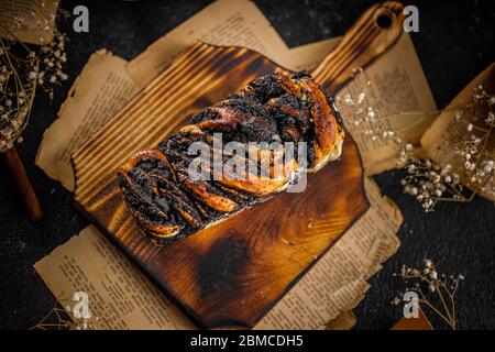 Stillleben von Babka Kuchen oder Brioche mit Mohn Samen auf dem alten Holzteller, leckeres Wirbel Brot Stockfoto