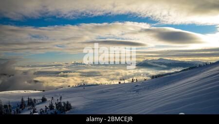 Luftaufnahme über den Wolken auf schneebedeckten Berggipfeln, die von der Sonne beleuchtet werden Stockfoto