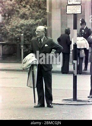 Ein älterer Mann in einem Anzug wartet auf ein Taxi oder hackney Taxi auf einer Straße in Manchester, England, Großbritannien im Jahr 1974. Stockfoto