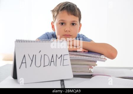 Müde frustrierte Junge am Tisch mit vielen Büchern sitzen. Das spanische Wort Auydame - Help Me- steht auf offenem Notizbuch Stockfoto
