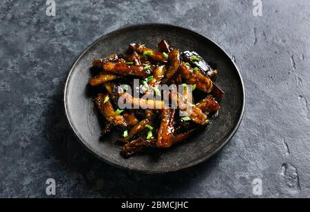 Nahaufnahme von gebratener Aubergine im koreanischen Stil. Bulgogi Aubergine auf Teller über dunklem Steingrund braten. Stockfoto