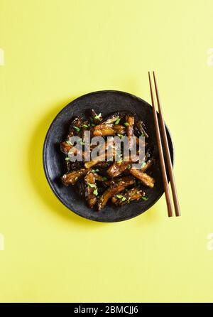 Braten Bulgogi Aubergine auf Platte über gelbem Hintergrund mit freier Textzähe. Gebratene Aubergine im koreanischen Stil. Draufsicht, flaches Lay Stockfoto