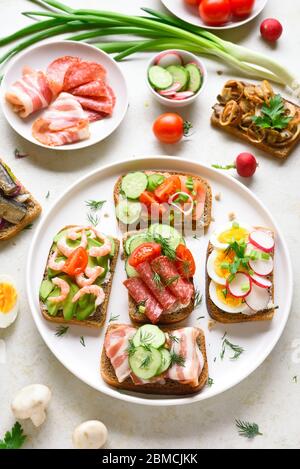 Auswahl offener Sandwiches auf Teller über hellem Steinhintergrund. Stockfoto