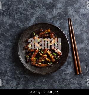 Gebratene Aubergine im koreanischen Stil. Bulgogi Aubergine auf Teller über dunklem Steingrund braten. Draufsicht, flaches Lay Stockfoto