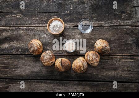 Frisch gebackene hausgemachte Brötchen und seine Zutaten - Mehl, Wasser und Sauerteig Vorspeisenhefe, platziert, um ein lächelndes Gesicht zu bilden. Stockfoto