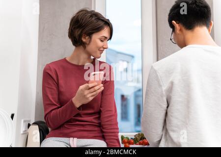 Foto von lächelndem multinationalen Paar mit Handy und Kochen Abendessen in der Küche zu Hause Stockfoto