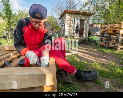 Ältere kaukasische Frau montiert einen Holzrahmen eines Gebäudes mit Metallbefestigungen mit einem Schraubendreher Stockfoto