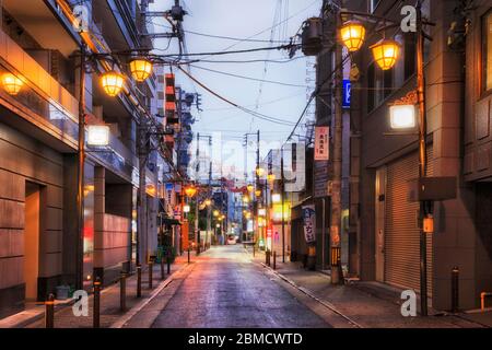 Osaka, Japan - 26 Dez 2019: Ruhige Hintergasse in der Innenstadt von Osaka bei Sonnenaufgang mit Straßenlaternen und verschlossenen Türen lokaler Unternehmen. Stockfoto