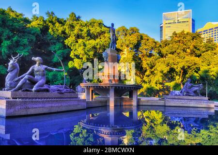 Innenstadt von Sydney im Hyde Park um stilles Wasser von Brunnen gegen blauen Himmel von Bäumen umgeben. Stockfoto