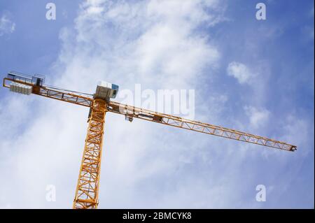 In den blauen Himmel ragt ein elektrischer Baukran. Gelber Turmkran mit Ausleger, Kabine und Gegengewicht fotografiert gegen blauen Himmel. Stockfoto