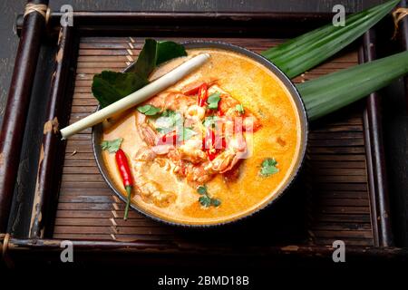 Garnelen Tom Yam Kung in grauer Schale mit thailändischen Gewürzen auf autentischem Tablett Draufsicht, Holzhintergrund Stockfoto