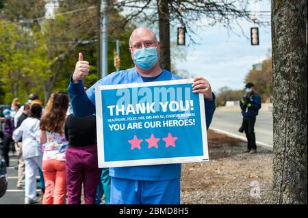 Gesundheitsarbeiter, die während der National Nurses Week Maske und Peelings tragen und den Daumen hoch halten, während er ein Schild hält, das unseren Helden dankt. Stockfoto