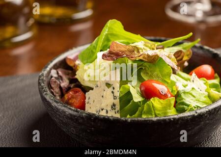 Salat mit grünem Salat und grünen Blättern mit blauem Käse und Tomaten auf einer Schüssel auf einer Ledertischmatte und einem verschwommenen Hintergrund mit Olivenöl A gesetzt Stockfoto