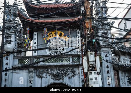 Hanoi Vietnam Oktober 24 2013; typisch asiatisches Gewirr von Stromleitungen vor dem Gebäude der traditionellen asiatischen Architektur. Stockfoto