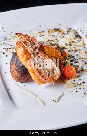 Schweinefleisch am Knochen mit gebackenen Kartoffeln, dekoriert mit eingelegten Kirschtomaten. Fotos für Café- und Restaurantmenüs Stockfoto