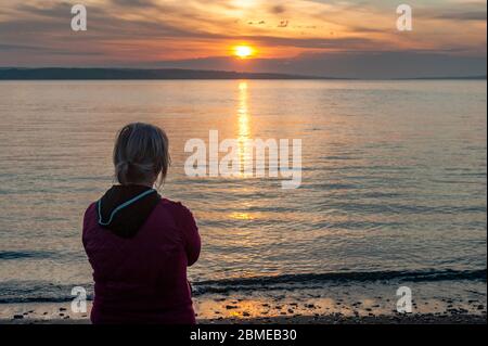 Courtmacsherry, West Cork, Irland. Mai 2020. Aufgrund der Covid-19 Lockdown musste Pieta House dieses Jahr seinen Darkness Into Light Walk abbrechen. Pieta House drängte jedoch die Leute, den Sonnenaufgang zu sehen, um Geld für die Wohltätigkeitsorganisation zu sammeln. Eine Frau beobachtet den Sonnenaufgang am Broadstrand Beach. Credit: AG News/Alamy Live News Stockfoto