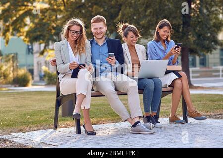 Lächelnde Business junge Menschen auf Bank im Park, arbeiten auf Laptop, SMS-Nachricht. Stockfoto