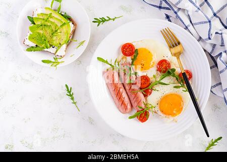 Englisches Frühstück - Spiegeleier, Würstchen, Tomaten und Rucola. Amerikanische Küche. Ansicht von oben, Overhead, Kopierbereich Stockfoto