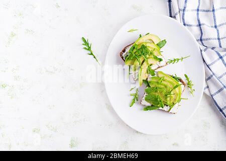 Sandwich von Frischkäse Brot und Scheiben Avocado auf einem Teller auf einem hellen Hintergrund. Gesundes vegetarisches Essen. Ansicht von oben, Overhead, Kopierbereich Stockfoto