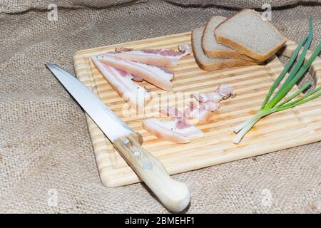 Geräucherter Speck, Brot, grüne Zwiebel auf einem Holzbrett. Stockfoto