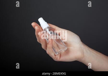 Antibakterielle Sprühflasche in der Hand auf dunklem Hintergrund Nahaufnahme. Antiseptisch, Hygiene. Stockfoto