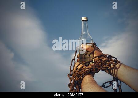 Hand an eine Flasche Alkohol gefesselt, gegen den blauen Himmel. Stockfoto