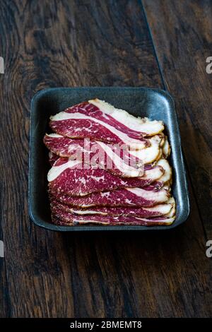Roh geräuchert trocken gereiften Kalbsrippe Scheiben in Kunststoff-Container-Box-Paket zum Verkauf. In Scheiben geschnitten und geschnitten Schinken / Salami. Bereit zum Essen. Stockfoto