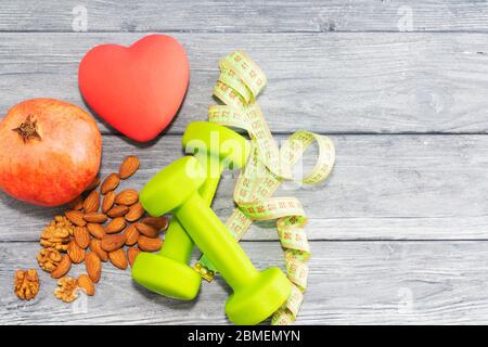 Granatapfel, Hanteln, Maßband auf dem Hintergrund einer Holzstruktur. Fitness, Sporternährung. Stockfoto