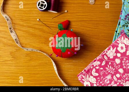 Verschiedene Nähzubehör sitzen auf einem hölzernen Hintergrund. Im Bild kann man ein Nadelkissen mit eingestockten Stiften, Faden, verschiedene Bettwäsche und ein Klebeband sehen Stockfoto