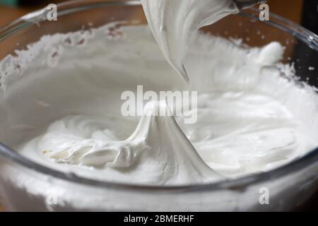 Baiser in einer klaren Glasschale bilden eine steife Spitze in der Mitte, wie der Mixer aus den gemischten Zutaten entfernt wird Stockfoto