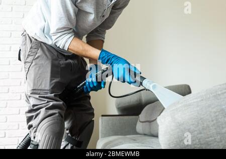 Mann-Mitarbeiter des Trockensaugers entfernt Schmutz von Möbeln in flachen, Nahaufnahme, Staubsauger sauber Sofa mit professioneller Ausrüstung Stockfoto